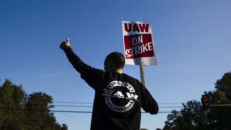 A worker gives the thumbs-up gesture to a passing motorist as he demonstratives outside a...